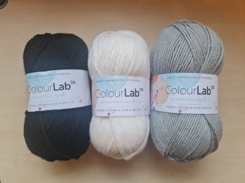 A picture of three hanks of the yarn Colour Lab double knit by West Yorkshire Spinners in the colours Phantom Black, Arctic White and Silver Grey.